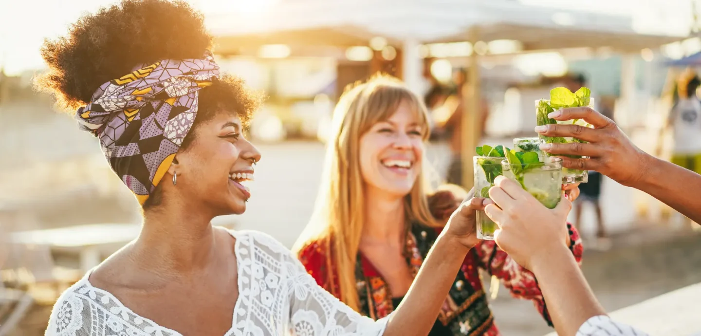 Three women joyfully toasting with drinks at an outdoor event, celebrating together in a vibrant atmosphere.